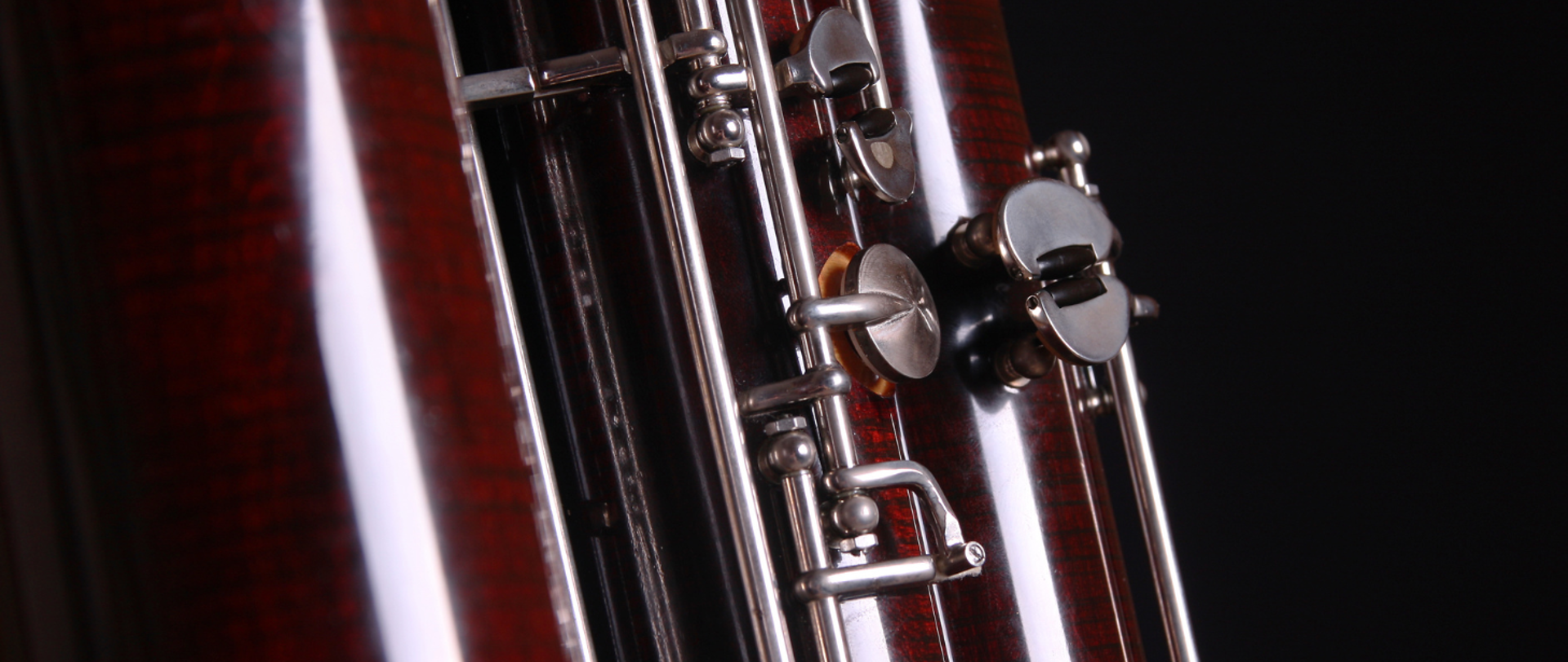 Kolorowe zdjęcie zbliżenie na niewielką część środkowej części fagotu z klapkami, znajdującego się na czarnym tle.