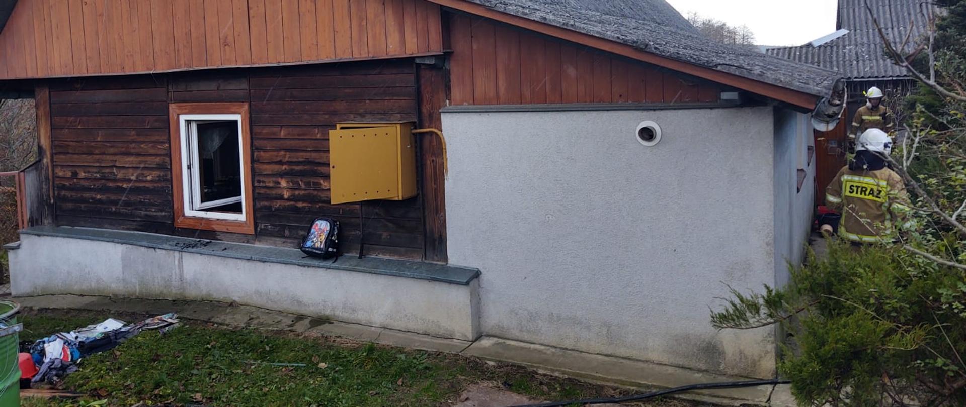 Widok budynku w którym powstał pożar oraz strażacy obok niego.