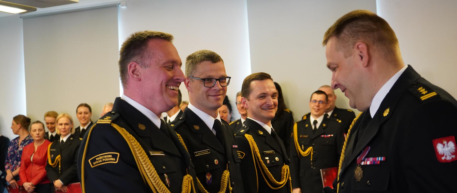 strażak ściska dłoń innemu strażakowi, w tle ludzie