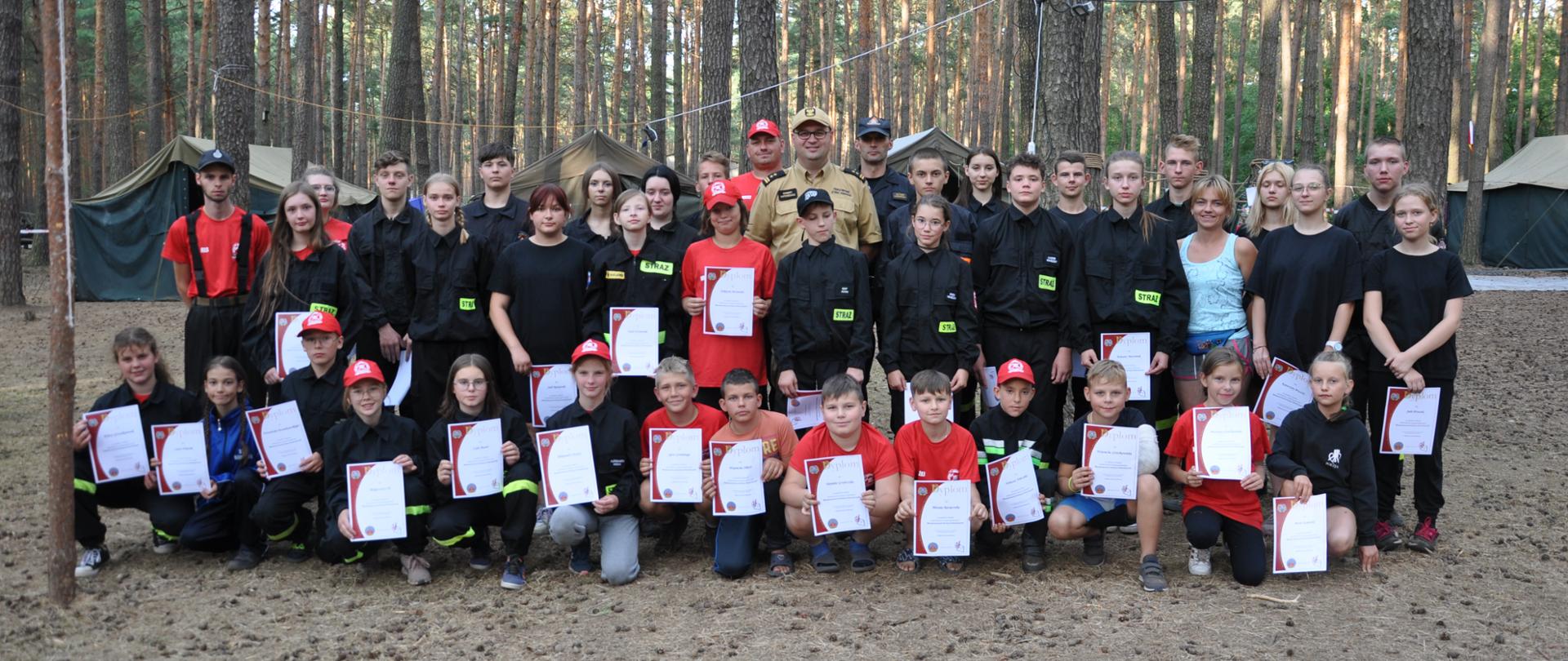 Obóz MDP Lgiń. Grupa ludzi, uczestników obozu wspólnie pozuje do pamiątkowego zdjęcia, w tle drzewa i namioty.