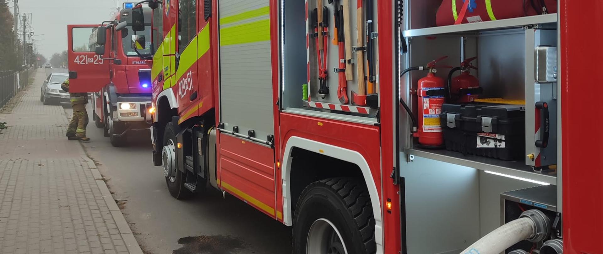 Na zdjęciu widać bok samochodu pożarniczego biorącego udział w akcji gaśniczej. Do samochodu podłączona jest wąż gaśniczy