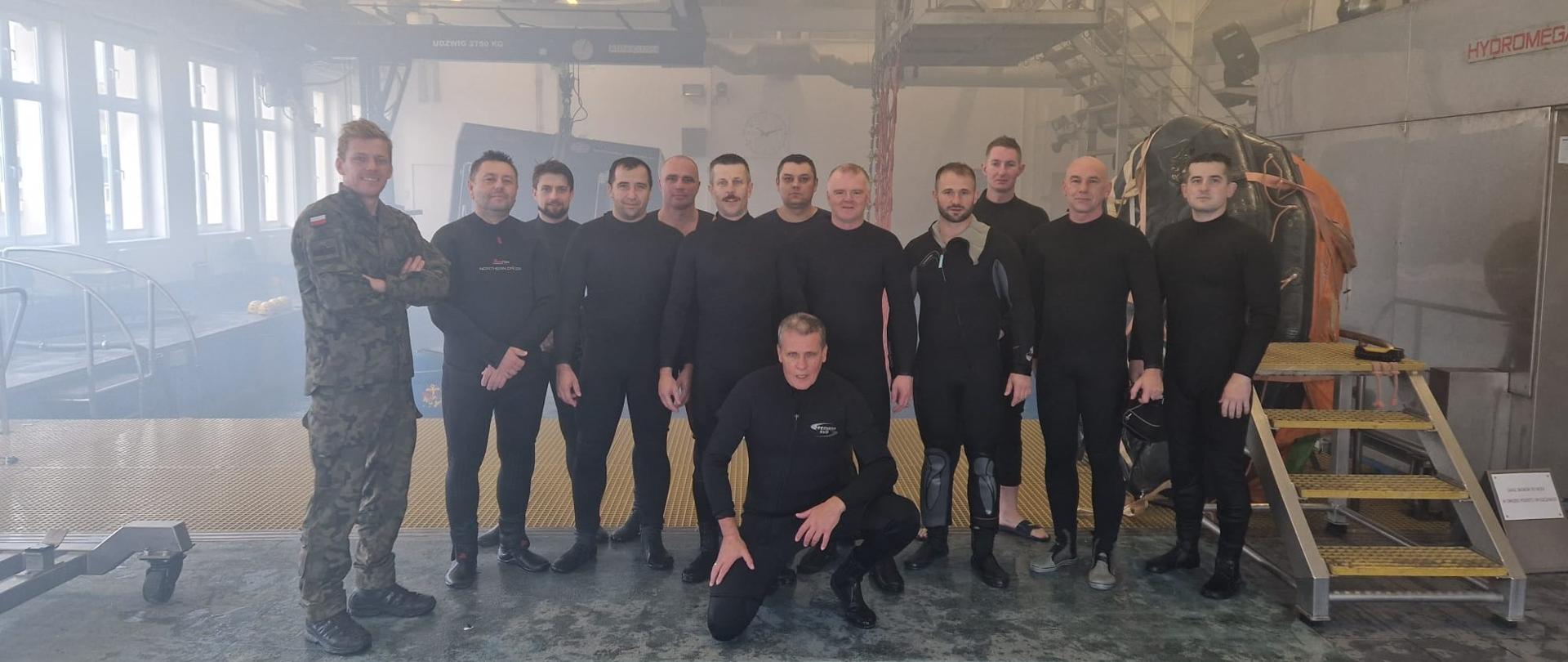 Grupa 13 mężczyzn uczestników szkolenia pozuje do zdjęcia grupowego na tle basenu