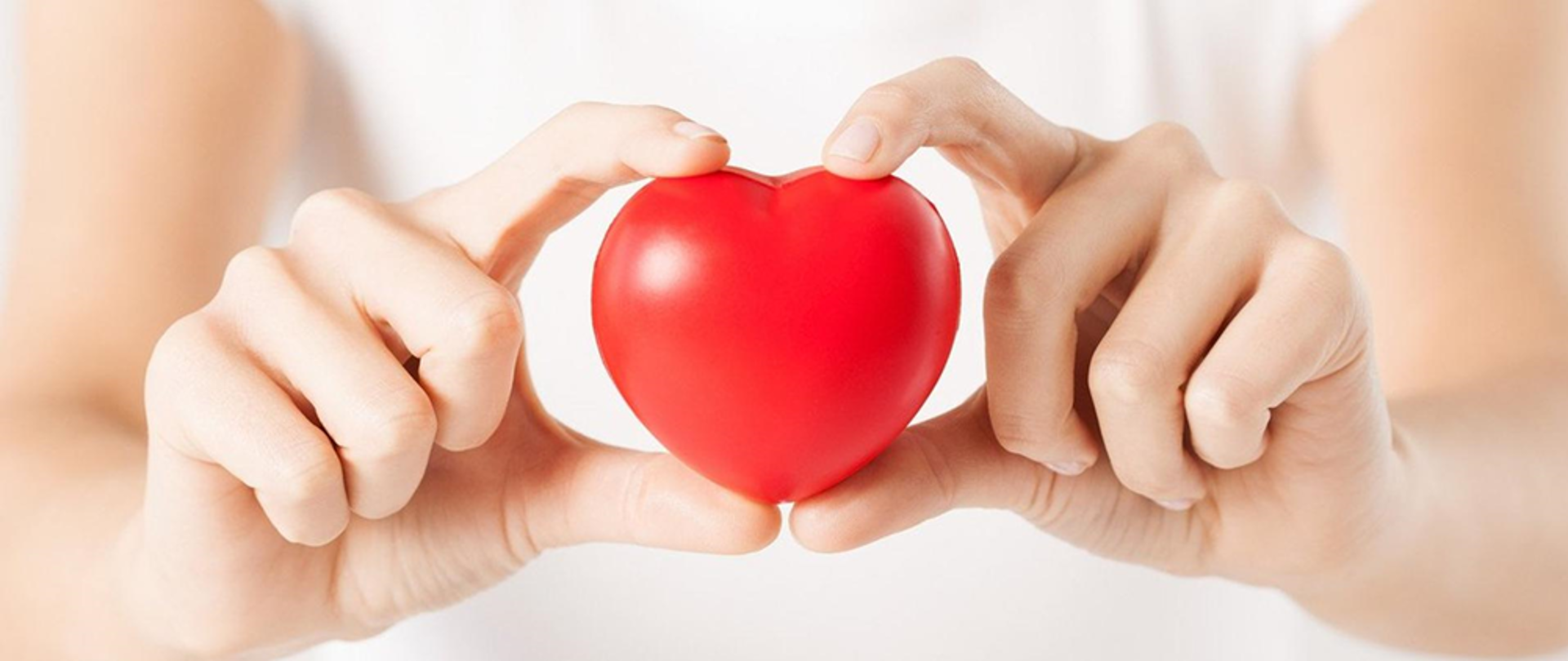 Czerwone gumowe serce trzymane palcami dłoni.
