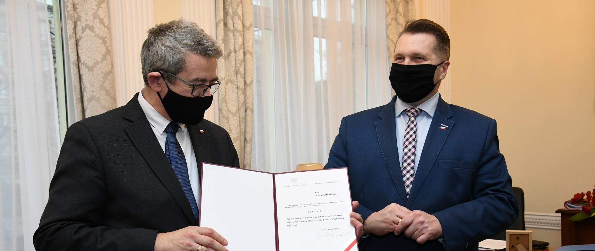 Wojciech Murdzek pokazuje nominację, obok stoi minister Czarnek.