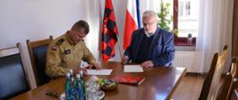 Komendant Państwowej Straży Pożarnej i burmistrz Czarnkowa Jacek Klimaszewski podpisują dokumenty przy stole konferencyjnym, w tle widoczne flagi Polski, UE i miasta.