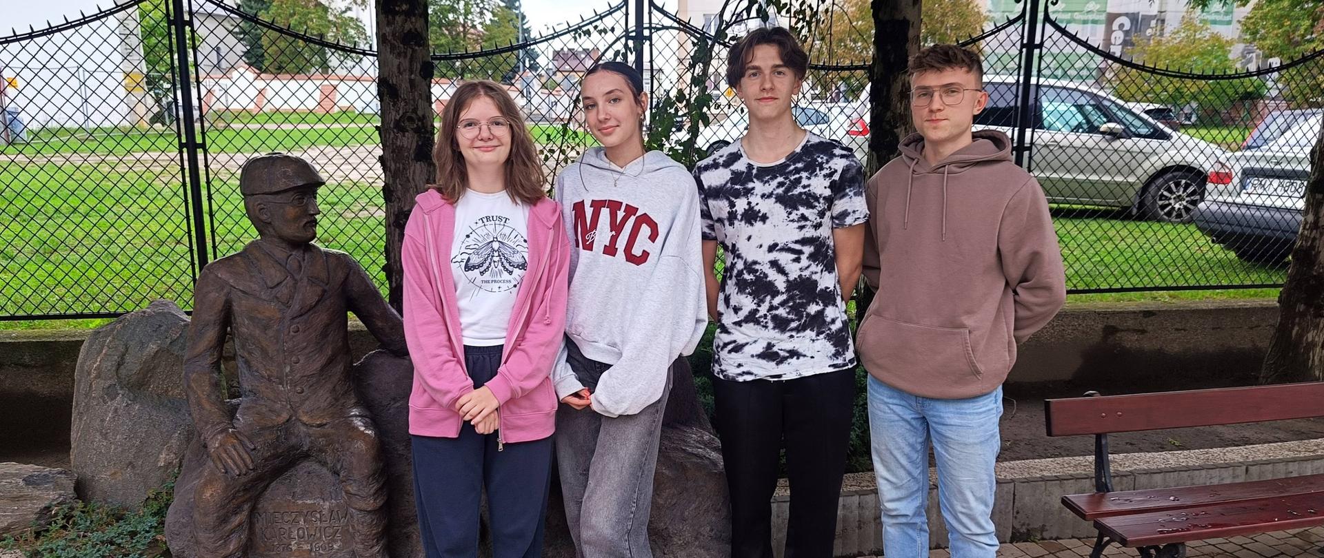 Czworo uczniów stojących obok pomnika siedzącej postaci, wybranych do Samorządu Uczniowskiego.