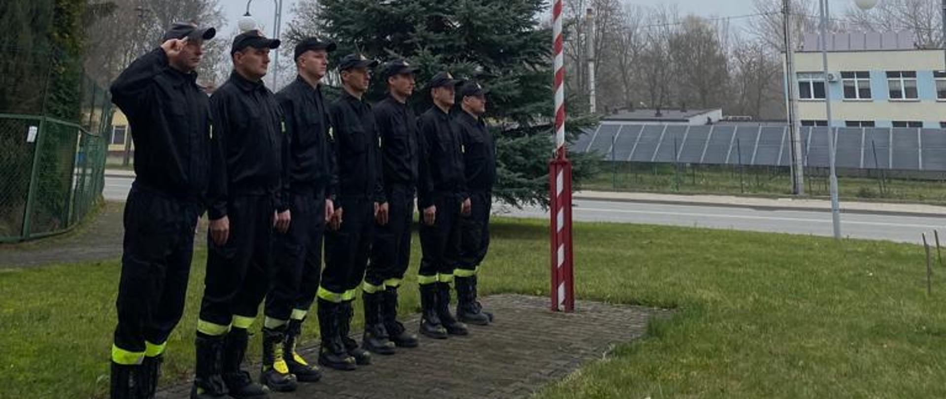 na zdjeciu widoczni straacy na dle masztu z flagą