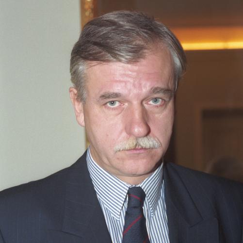 Andrzej Olechowski kolorowy portret mężczyzny, siwe włosy, wąsy, granatowa marynarka w paski, granatowy krawat w czerwone paski, biała koszula w granatowe paski.