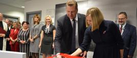 Minister Czarnek i kobieta w granatowym ubraniu przecinają nożyczkami czerwoną wstęgę, za nimi stoi grupa ludzi.