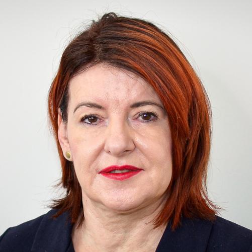 Kobieta w ciemnej marynarce, z kasztanowymi włosami, odsłoniętym jednym uchem.