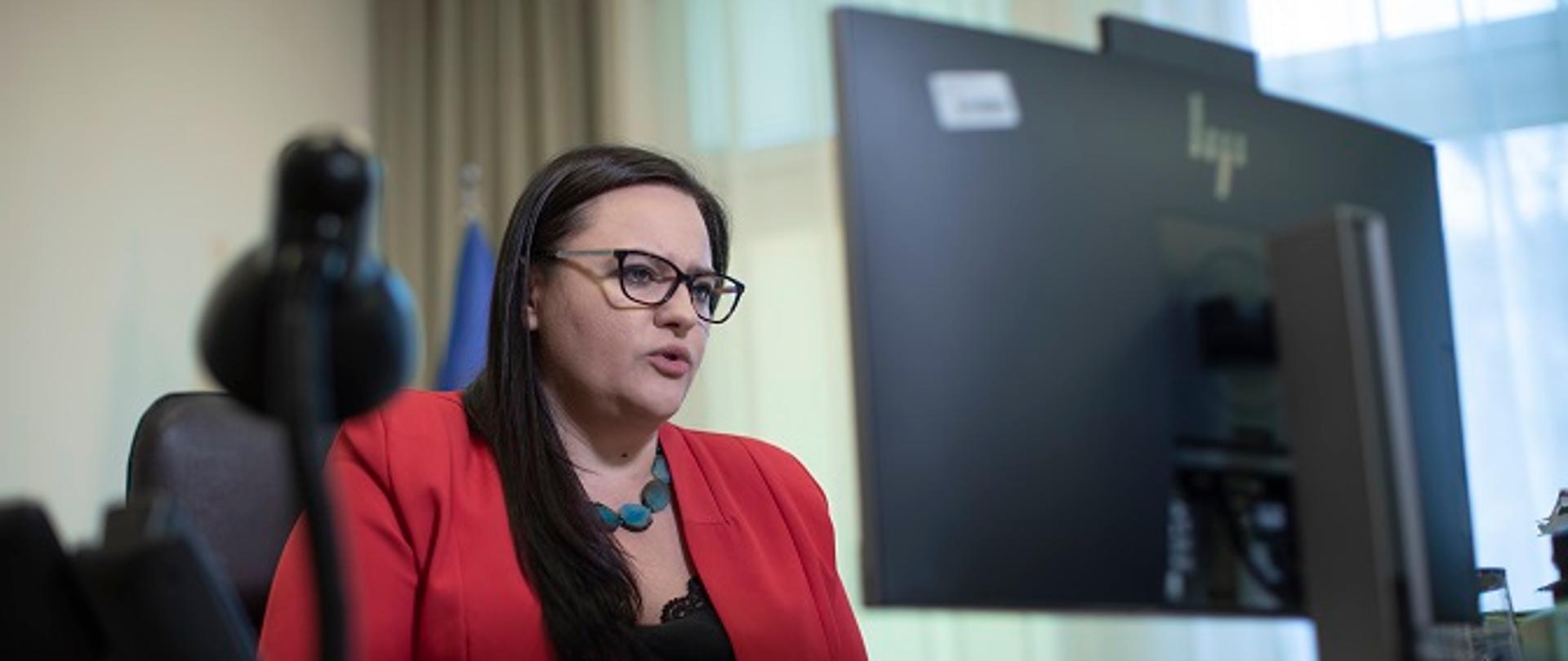 Minister Małgorzata Jarosińska-Jedynak siedzi przy biurku, przed komputerem. Trwa briefing prasowy.