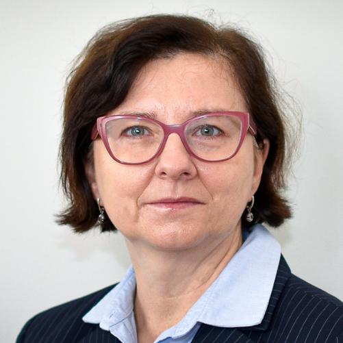 Kobieta w ciemnej marynarce w paski, jasnej bluzce i okularach, z krótkimi, ciemnymi włosami.