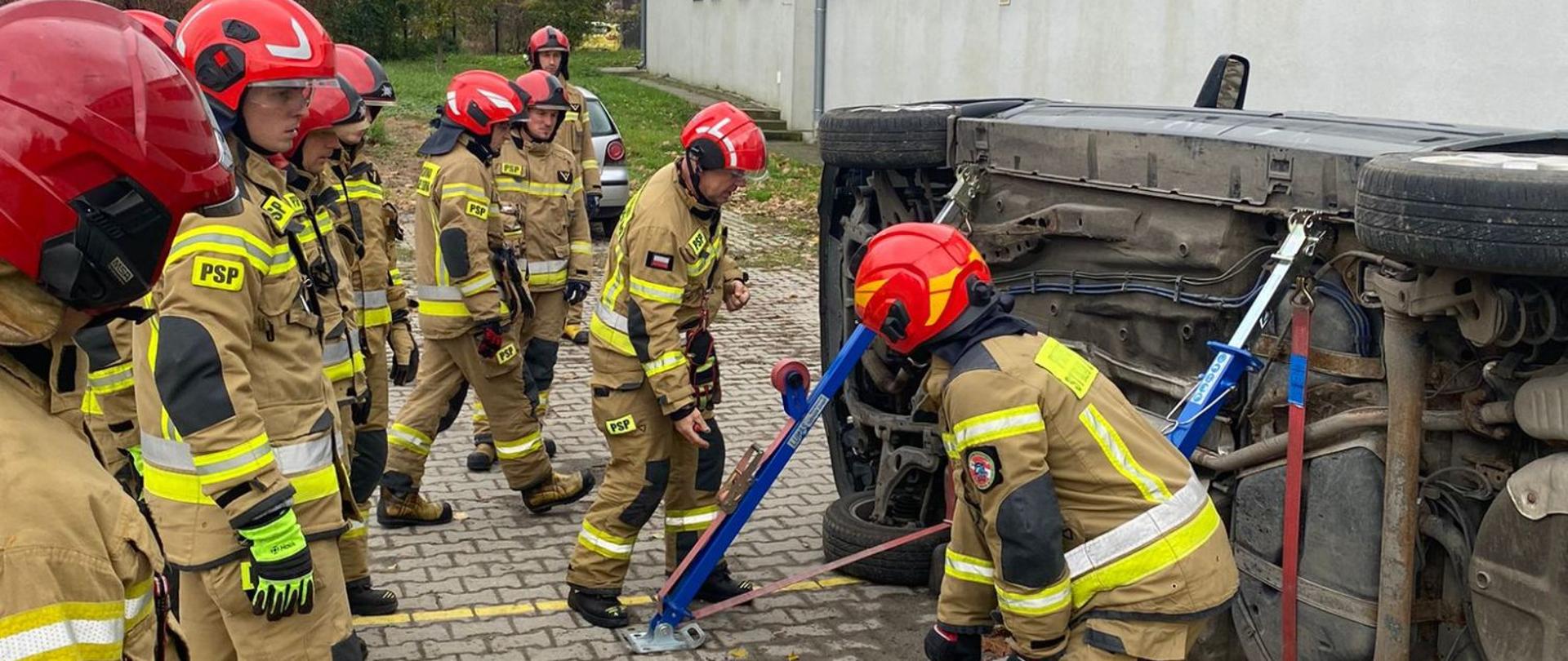 Strażacy Państwowej Straży Pożarnej podczas szkolenia doskonalącego z ratownictwa technicznego. Funkcjonariusze w umundurowaniu bojowym (specjalnym) ćwiczą działania ratownictwa technicznego - użycie podpór bocznych na pojeździe - na terenie poligonu Komendy Wojewódzkiej Państwowej Straży Pożarnej w Opolu.