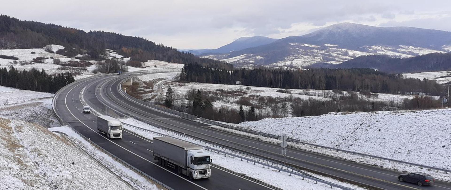 Widok na dwujezdniowy odcinek S7 z poruszającymi się pojazdami w obu kierunkach z przepięknym krajobrazem w tle.