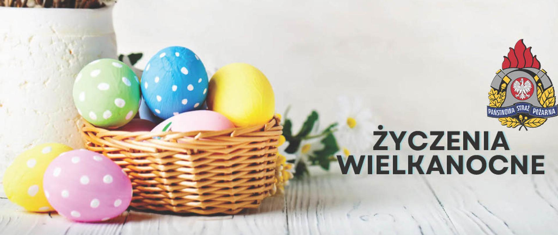 na zdjęciu po lewo widoczny koszyczek z kolorowymi jajkami po prawo logo straży i napis życzenia wielkanocne