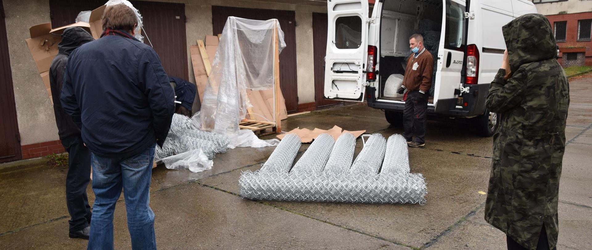 Osoby, które otrzymały pomoc odbierają siatki ułożone na ziemi i wkładają je do samochodu, z boku stoją pracownicy Regionalnej Dyrekcji Ochrony Środowiska.