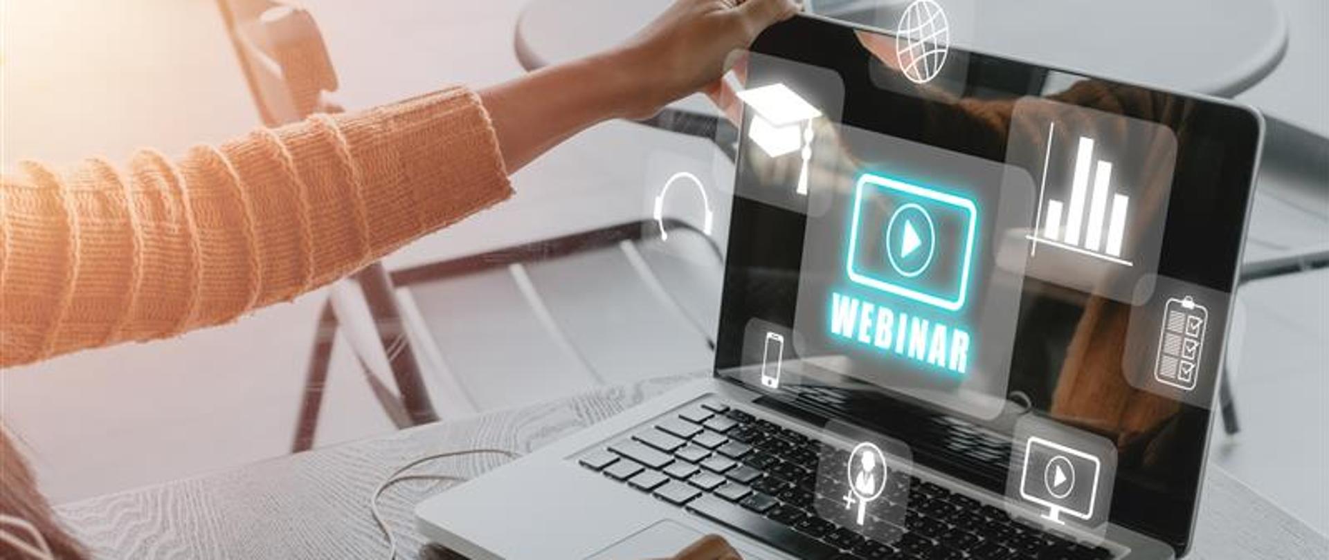 Osoba siedząca przy laptopie, widoczne ręce na klawiaturze. Na ekranie komputera napis webinar