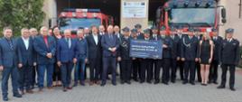 Grupowe zdjęcie strażaków OSp Gołuchów i zaproszonych gości osoby stoją w zwartej grupie strażacy stojacy w centrum trzymają baner Rządowego Funduszu Polski Ład przeznaczony dla inwestycji w Gminie Gołuchów