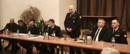 Zdjęcie przedstawia zastępce podkarpackiego komendanta wojewódzkiego podczas zebrania OSP. Obok siedzi burmistrz Ustrzyk Dolnych i zastępca komendanta powiatowego. Po drugiej stronie druhowie OSP. 