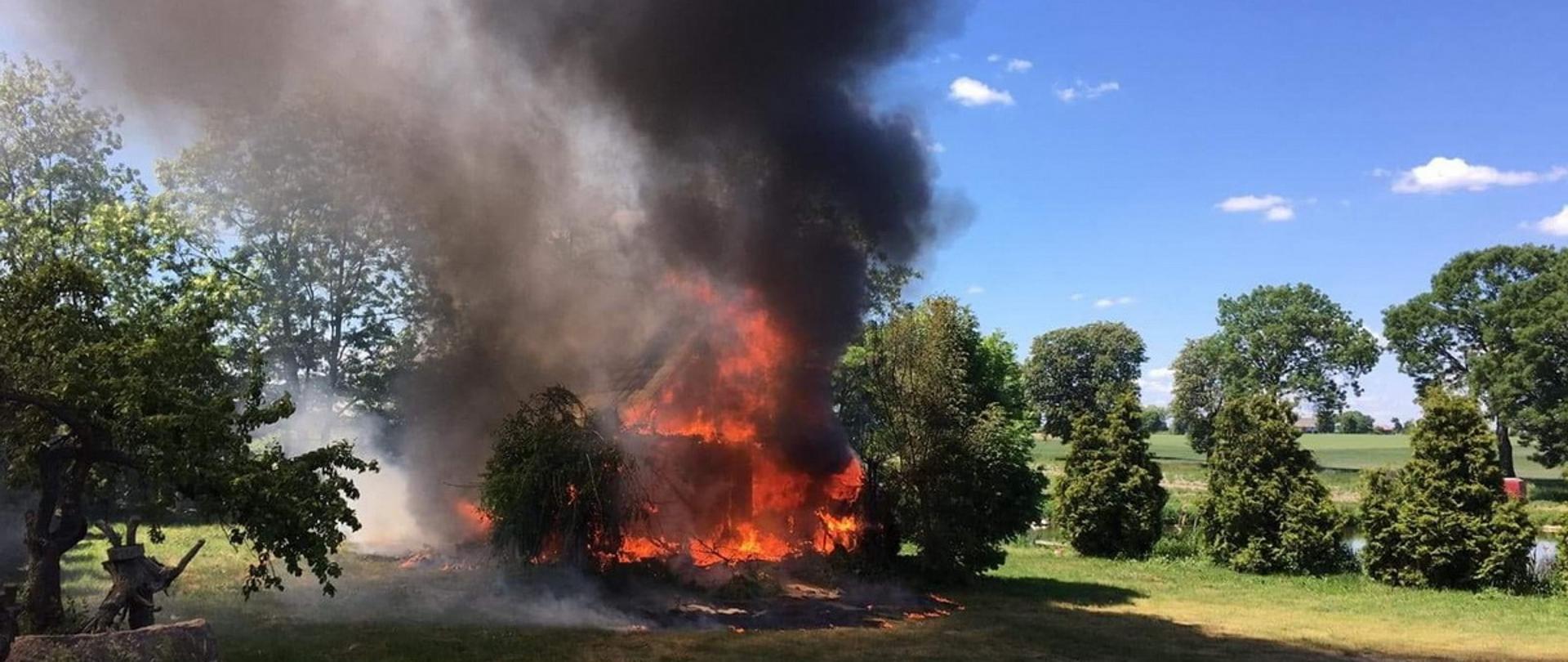Na zdjęciu widoczny jest budynek mieszkalny cały objęty ogniem. Nad nim unosi się ciemny gęsty dym. 