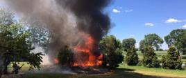 Na zdjęciu widoczny jest budynek mieszkalny cały objęty ogniem. Nad nim unosi się ciemny gęsty dym. 