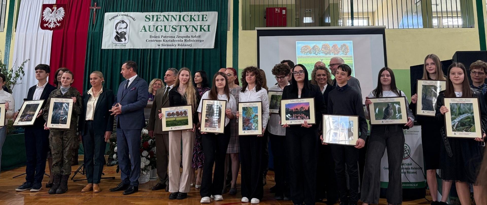 Zdjęcie grupowe laureatów konkursu z oprawionymi pracami, stojących na scenie.