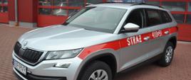 Na zdjęciu samochód lekki operacyjny marki Skoda Kodiaq na tle Komendy powiatowej PSP w Brzezinach. Samochód koloru srebrnego z oznaczeniami STRAŻ oraz numerem operacyjnym 410E91.