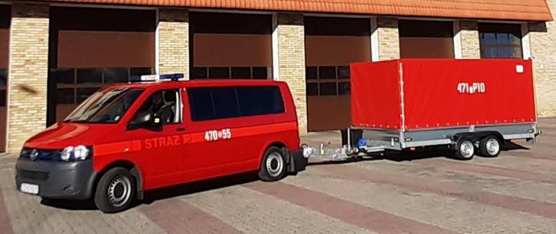 Czerwony samochód bus z przyczepą na tle remizy strażackiej