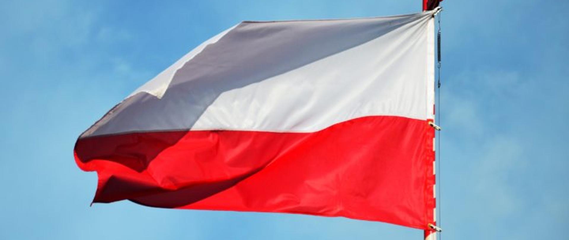 Biało-czerwona flaga zamocowana na maszcie powiewa na wietrze.