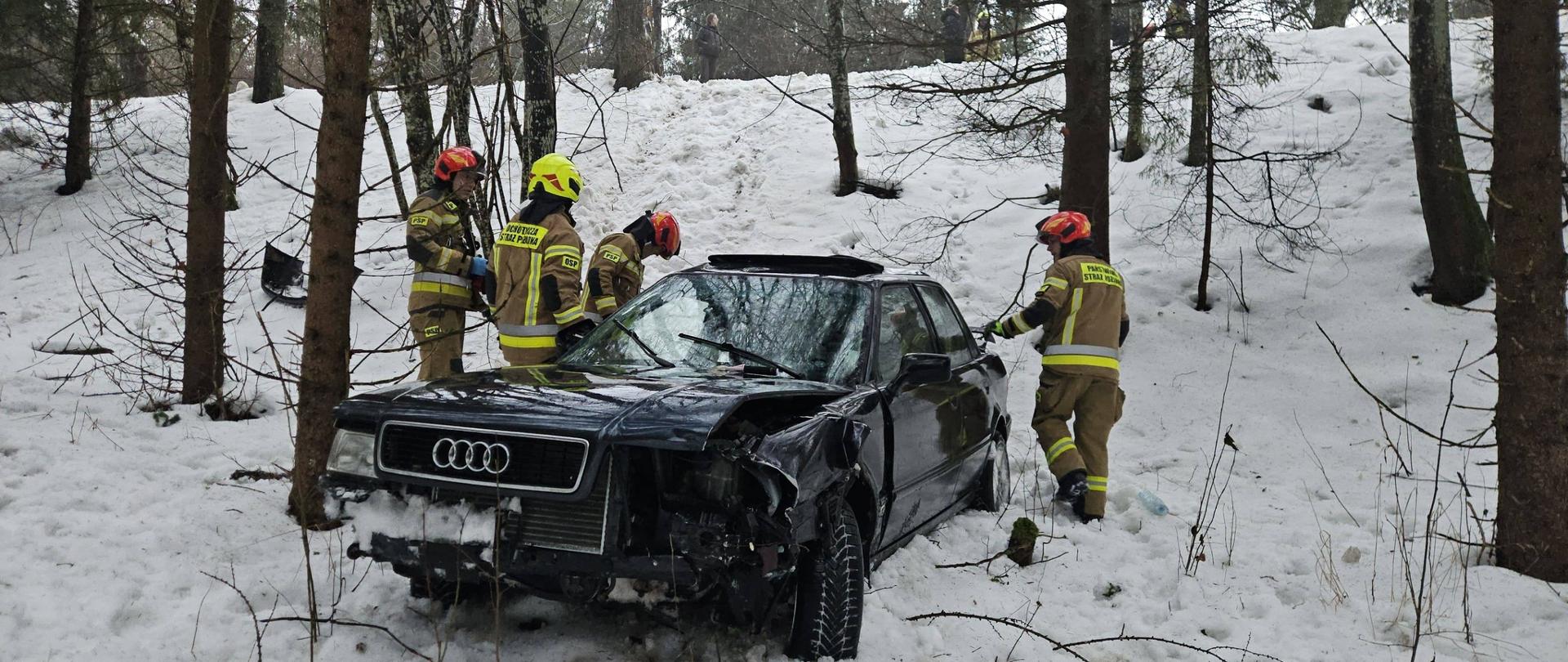 Ciemne auto osobowe poza drogą, przy nim czterech strażaków . Dużo śniegu.