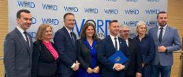 Grupa oficjeli, w tym wicewojewoda, stoją pozując do zdjęcia na tle ścianki z napisem WORD