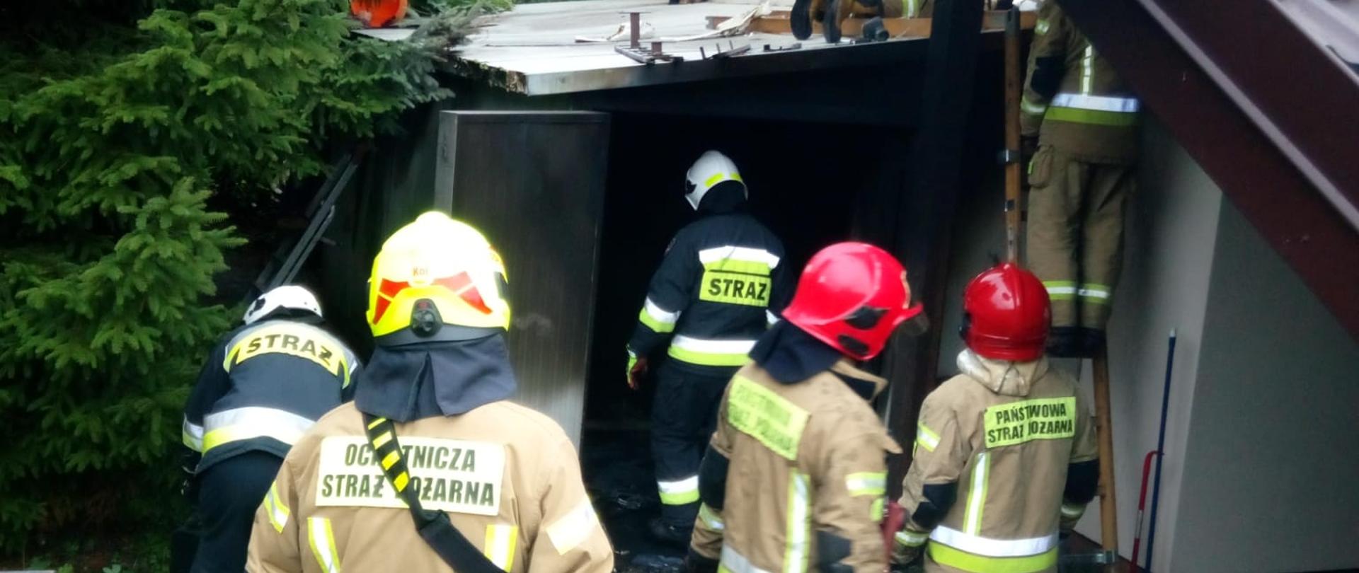 Zdjęcie przedstawia budynek gdzie doszło do pożaru. Po lewej widać kotłownię z płyt warstwowych, a przed jej wejściem znajduje się grupa strażaków. Ogień został już ugaszony, a ratownicy sprawdzają miejsce pożaru.