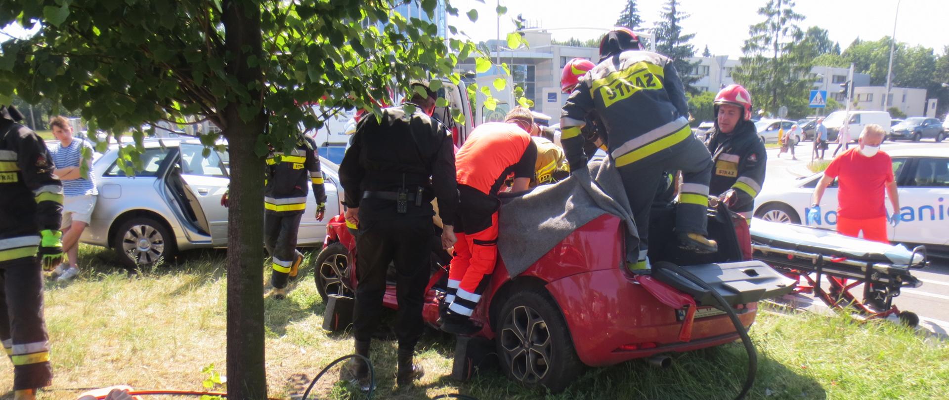Na zdjęciu widoczny jest uszkodzony samochód osobowy, strażacy odcięli dach pojazdu, przed samochodem widoczny jest sprzęt hydrauliczny