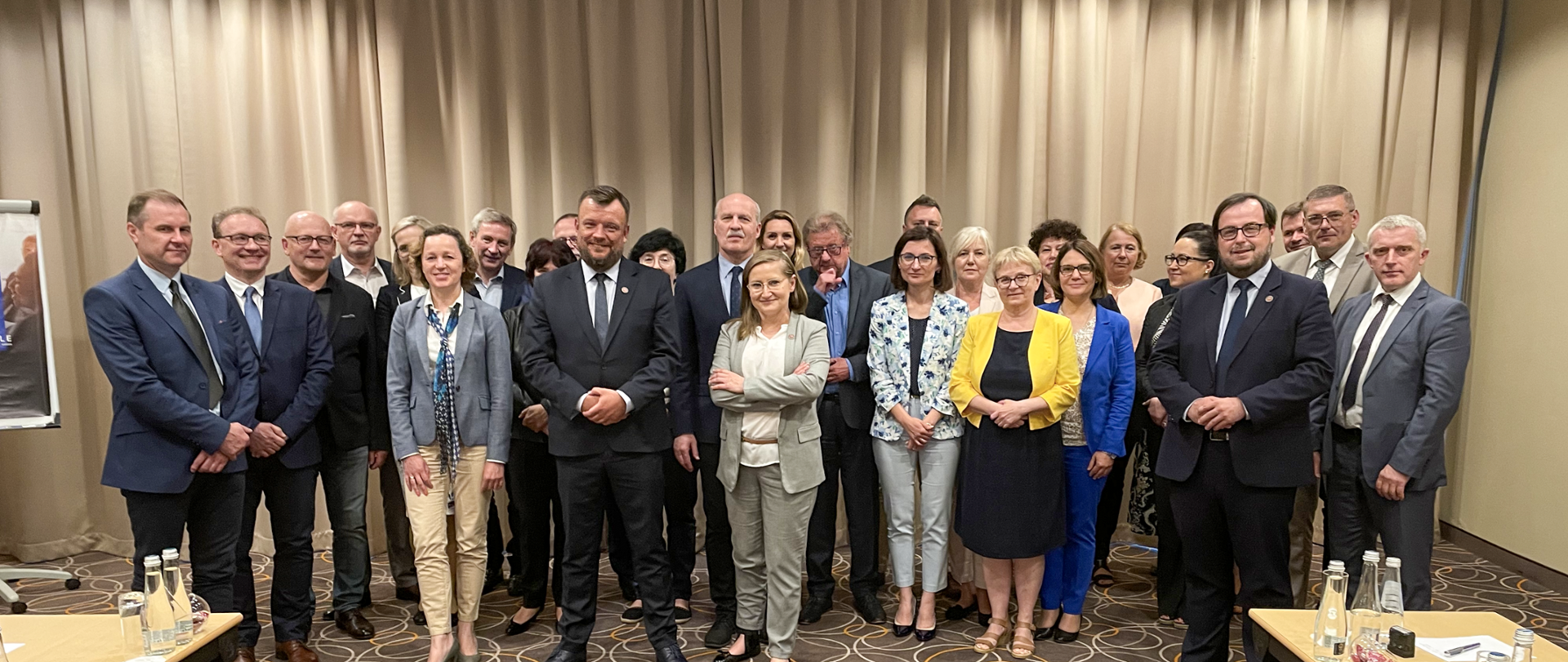 Grupa osób pozująca do zdjęcia na tle beżowych zasłon