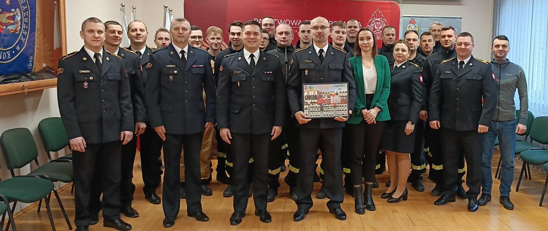 Na zdjęciu widać zgromadzonych funkcjonariuszy w mundurach służbowych na świetlicy. W tle czerwony baner.