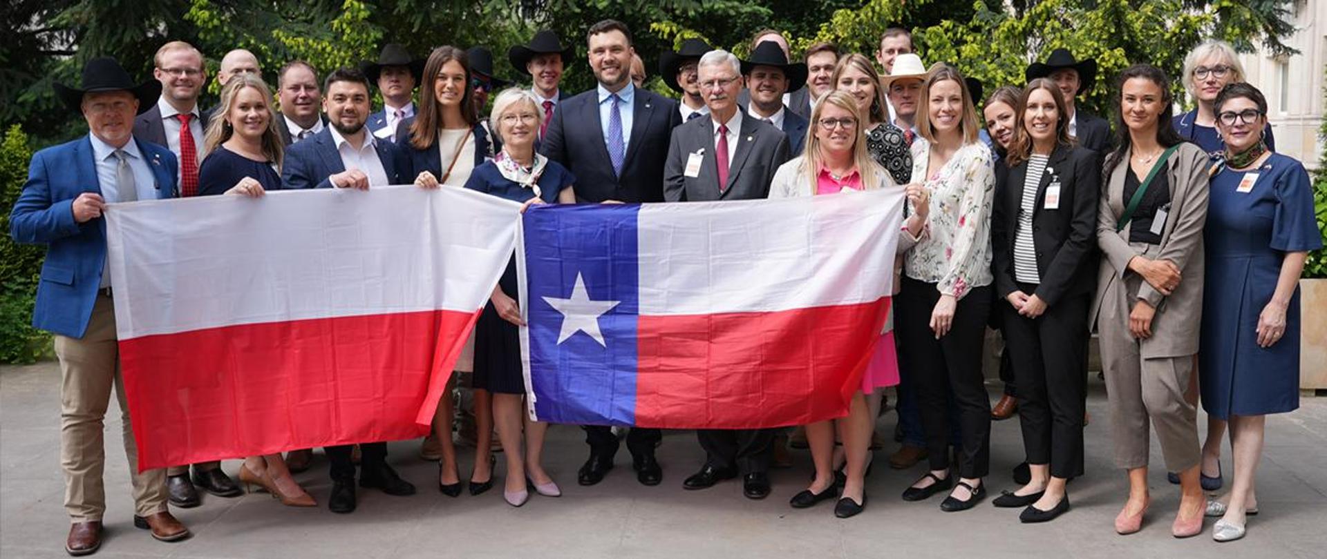 uczestnicy spotkania stojący na dziedzińcu MRiRW z flagami: Polski i stanu Texas