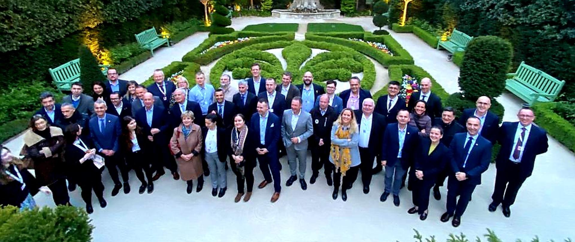 Plenerowe zdjęcie grupowe uczestników posiedzenia wykonane w ogrodzie. Ujęcie z góry wykonane z drona.