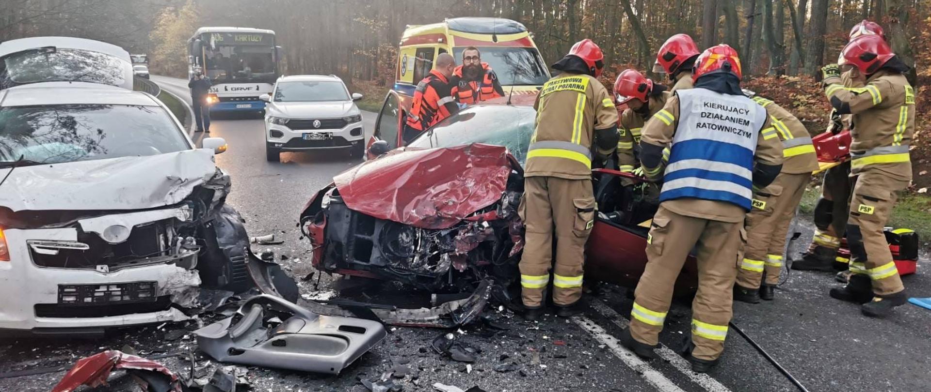 Strażacy prowadzący działania przy dwóch uszkodzonych pojazdach.