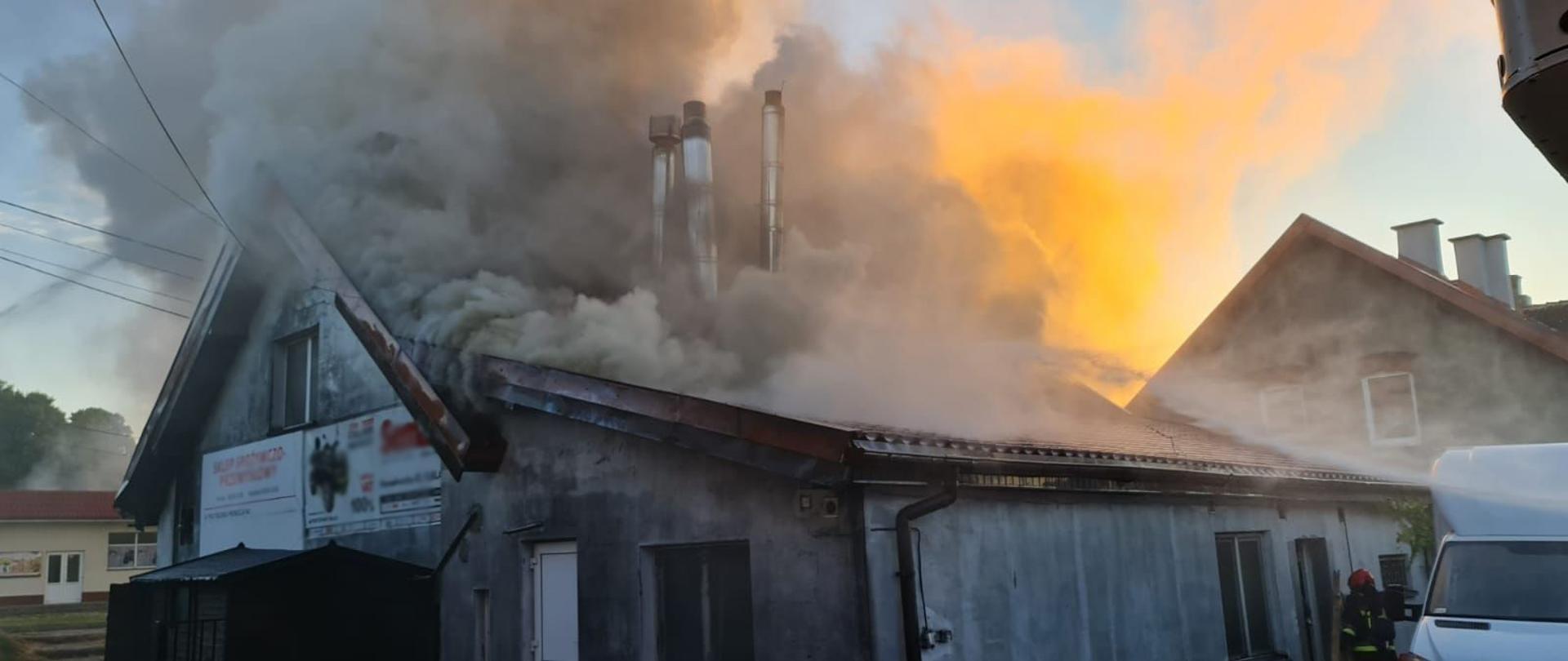 Budynek piekarni w centralnej części zdjęcia, z widocznymi kłębami dymu wydostającymi się z całej powierzchni poddasza.