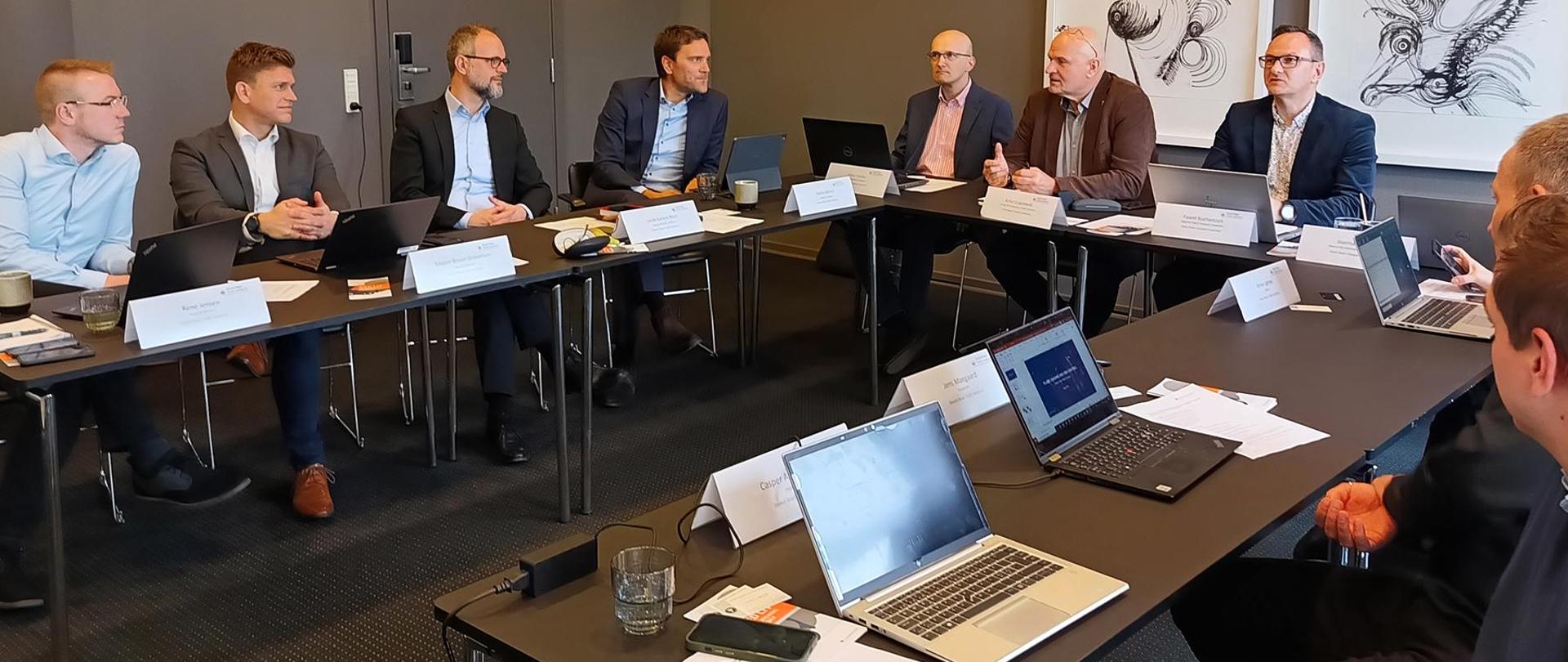 Mężczyźni siedzący za stołem w kształcie litery U