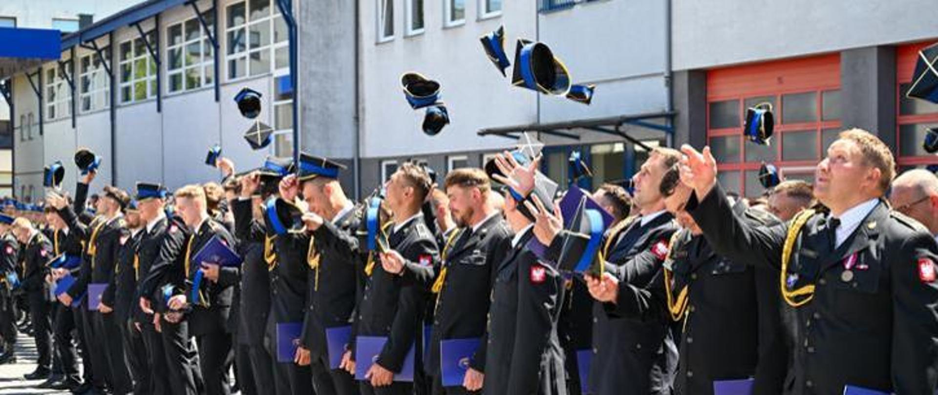 Zdjęcie z pormocji aspiranckiej. Strazacy stojący w pododziale otrzymali decyzje o awansie na stopien aspiranta. Strażacy podrzucają z radosci rogatywki. 