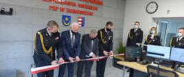 W pomieszczeniu czterech mężczyzn przecina wstęgę biało-czerwoną. Dwóch z mężczyzn to strażacy w umundurowaniu wyjściowym, w tym jeden w umundurowaniu generała, pozostali dwaj to osoby cywilne w garniturach. W pomieszczeniu widoczni są inni strażacy w umundurowaniu. W pomieszczeniu stoi biurko, na którym ustawiono monitory, przy biurku stoi fotel. Na ścianie widoczny napis "STANOWISKO KIEROWANIA KOMENDANTA MIEJSKIEGO PSP W TARNOBRZEGU". 