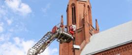 Zdjęcie przedstawia strażaka i rozstawiony podnośnik straży pożarnej w trakcie ćwiczeń na obiekcie kościoła św. Mikołaja w Wałczu 
