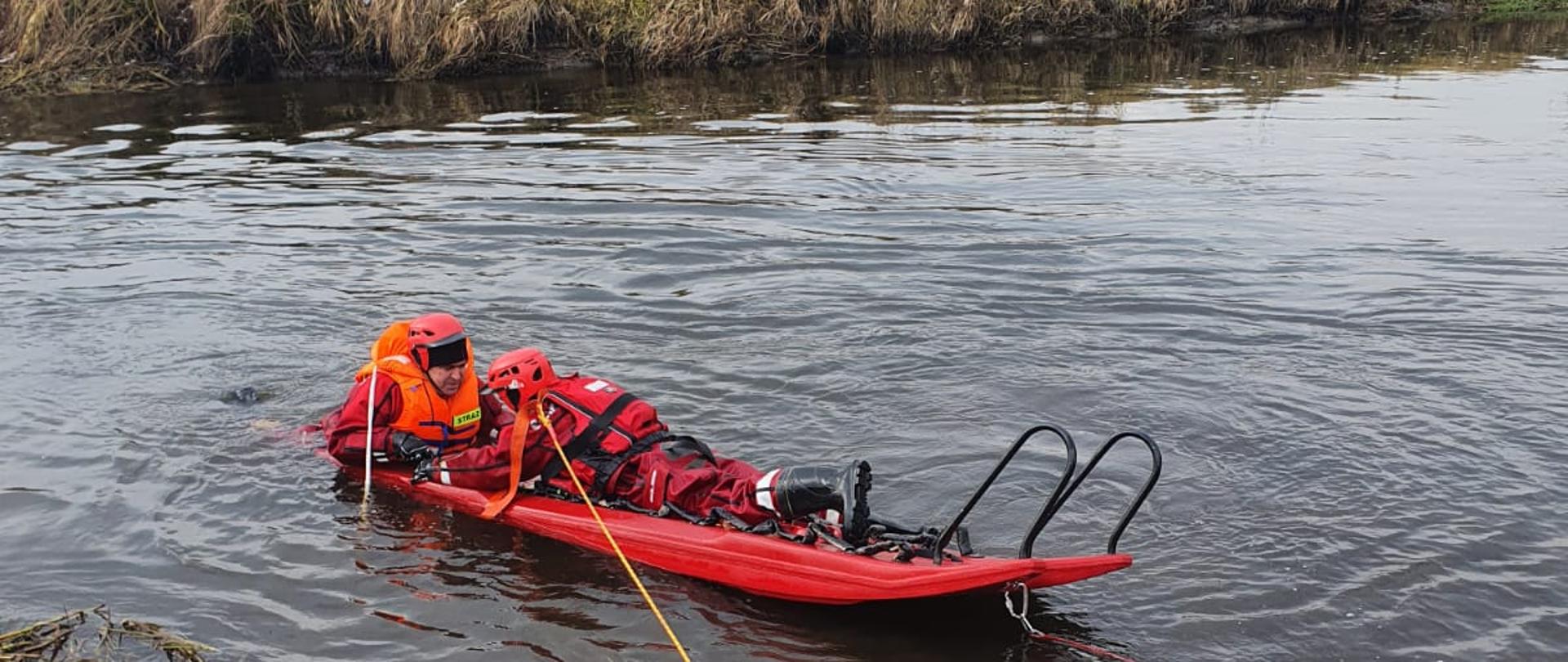 Dwóch strażaków na rzece wykonuje ćwiczenia z wykorzystaniem sań lodowych.