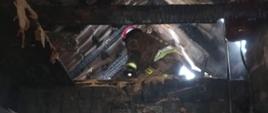 Na zdjęciu widoczny strażak pracujący w budynku mieszkalnym po pożarze poddasza, elementy wnętrza spalone, 