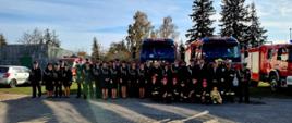 Strażacka społeczność gminy Grunwald i zaproszeni goście stoją przed samochodami pożarniczymi do pamiątkowego zdjęcia