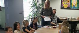 Dzieci zgromadzone wokół stołu słuchają prelegentki
