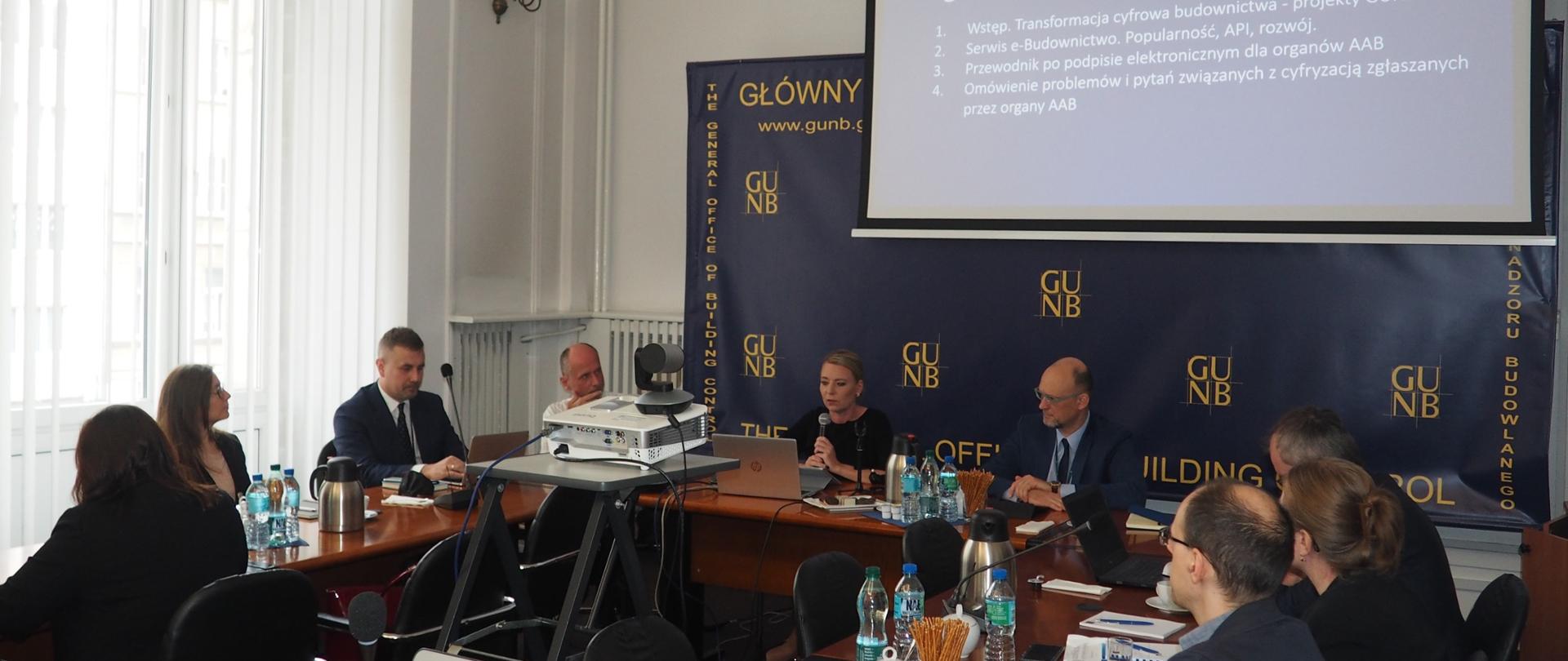 Prezentacja w sali konferencyjnej na temat cyfrowej transformacji budownictwa, z uczestnikami siedzącymi przy stole i slajdem agendy wyświetlanym na ekranie.