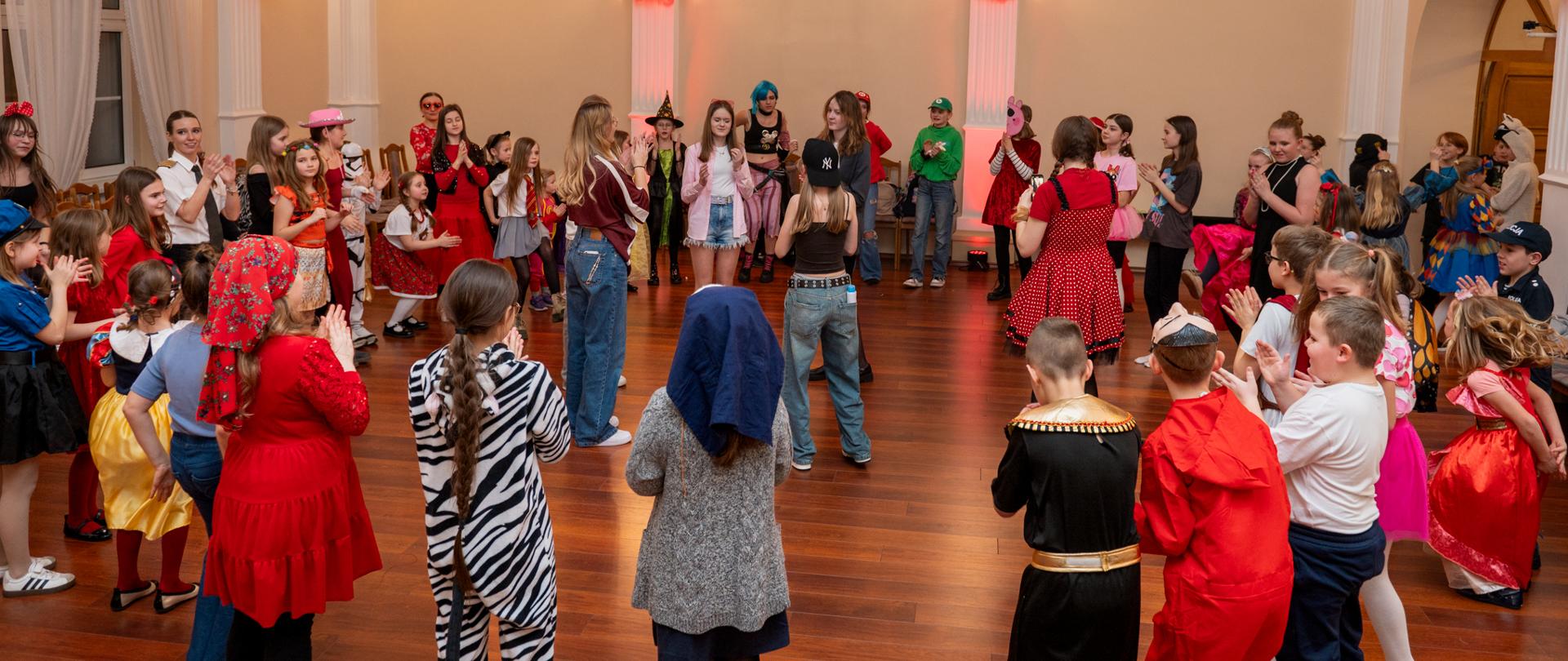 Grupa uczniów wraz z nauczycielkami tańcząca w auli Szkoły Muzycznej podczas Balu Karnawałowego