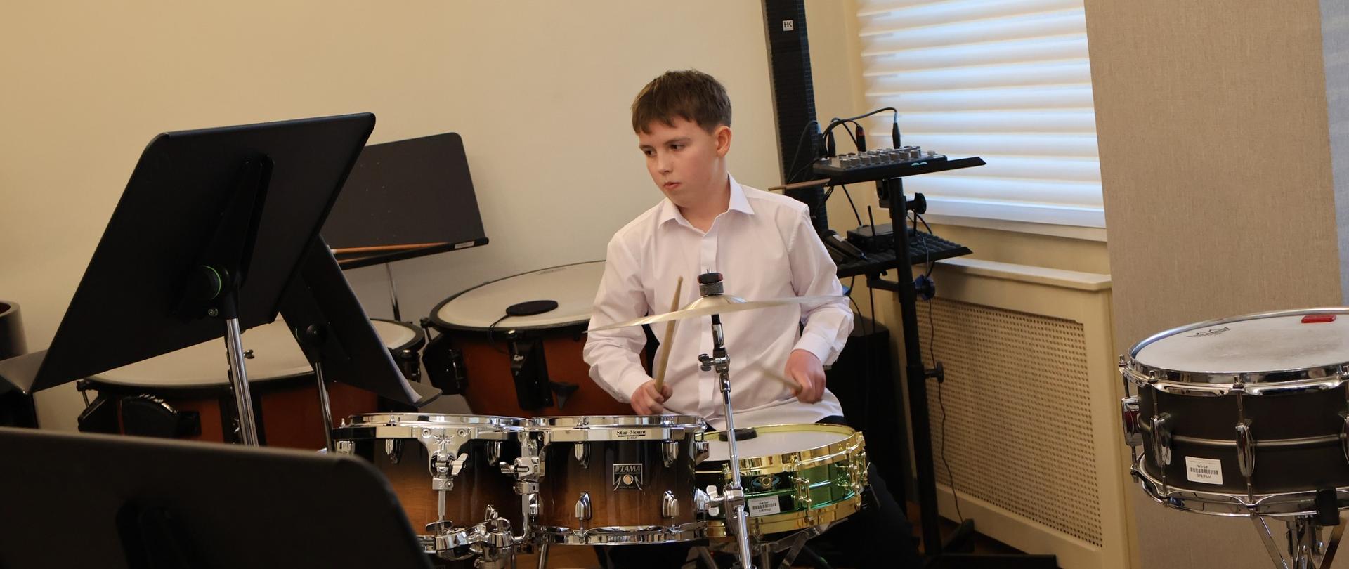 Uczeń w otoczeniu instrumentów perkusyjnych, gra na perkusji.